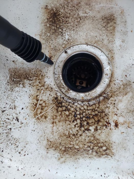 A dirty sink with a cleaning tool targeting grime and buildup around the drain