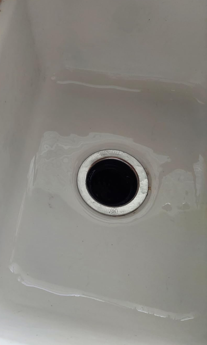 A close-up of a clean, empty white kitchen sink with a chrome drain