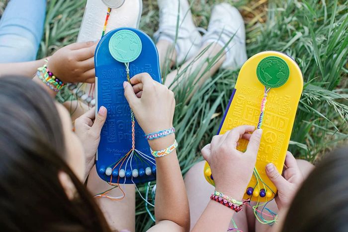 Two children models proudly wearing colorful friendship bracelets on their wrists while weaving more bracelets together