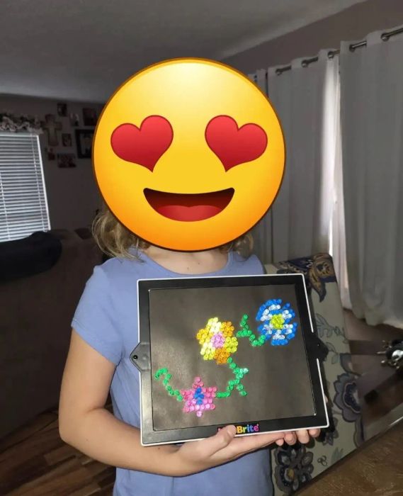 A reviewer shares a photo of their child holding a Lite-Brite with a flower design, with a heart-eye emoji covering their face.