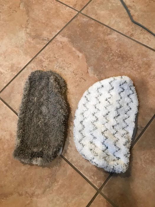 Two differently textured mop heads laid side by side on a tiled floor: one used and dirty, the other freshly cleaned.