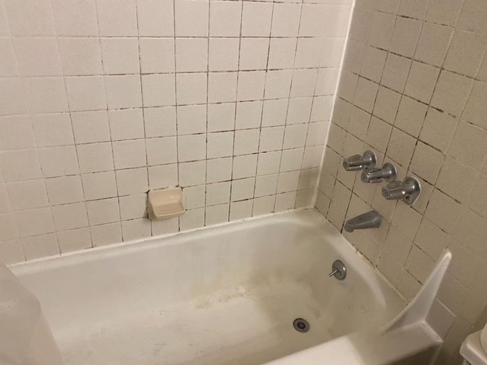 A reviewer's bathroom with a bathtub and chrome fixtures, featuring off-white tile walls with stained and discolored grout.