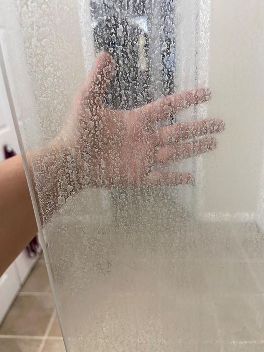 reviewer's hand behind glass shower door displaying hard water stains