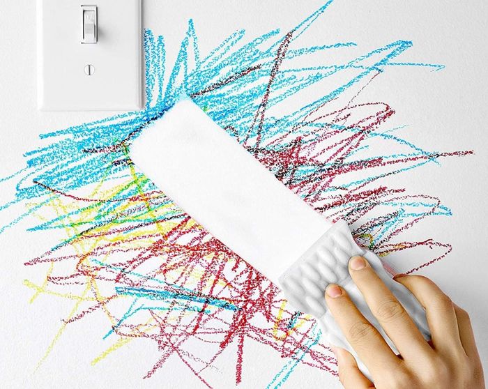 Someone using the sponge to remove crayon marks from a wall