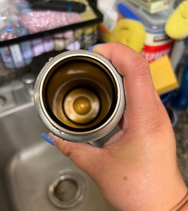 A before image showing a reviewer holding up a dirty stainless steel travel mug.
