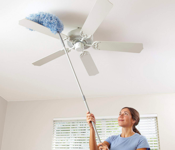 A person using the dusting pole to clean the top of a ceiling fan.