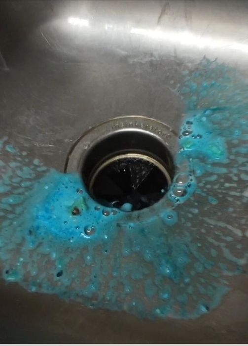 Blue foam draining from the sink into the disposal, with food particles visibly loosened.