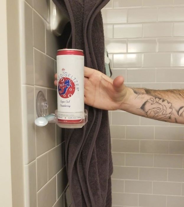 Reviewer grabbing a can from the holder mounted on a tile shower wall.