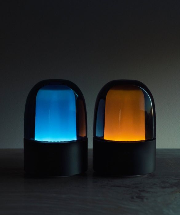 Two sleek LED lamps with glass domes, one glowing blue and the other orange, positioned on a dark surface.