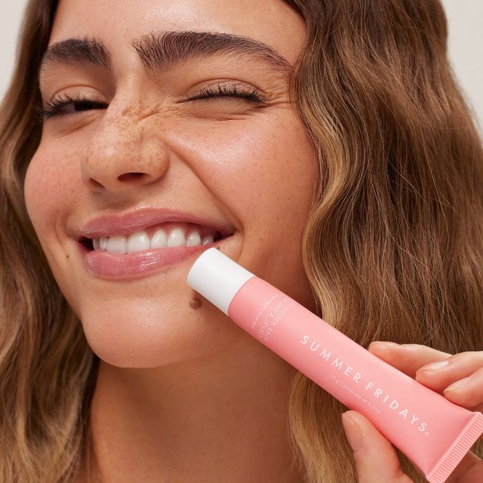 A person smiles while holding a Summer Fridays lip balm near their face, promoting beauty products.
