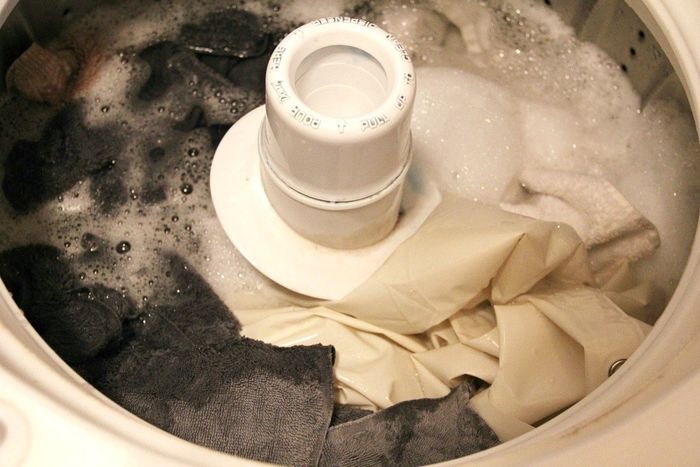 The shower curtain liner in a soapy washing machine along with towels.