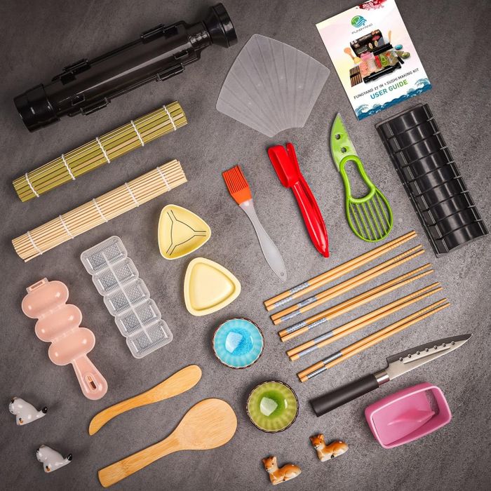 A sushi making kit displayed with various tools such as rolling mats, molds, chopsticks, spoons, a guidebook, and a knife. The set also includes soy sauce dishes and charming panda figurines.