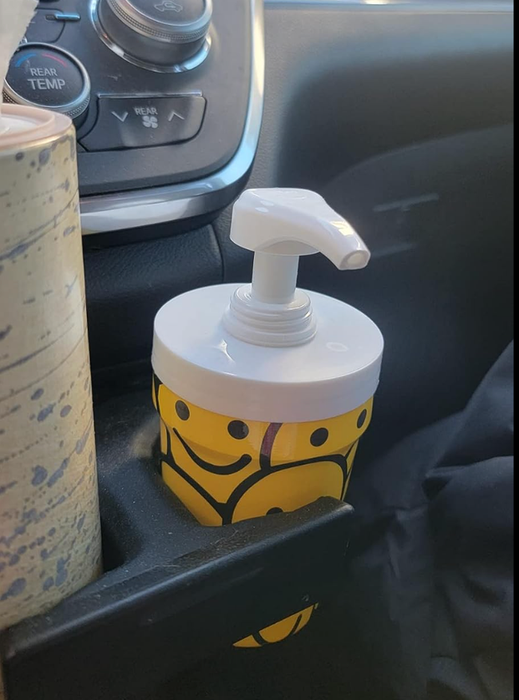 A cup with a smiley face pattern and a dispenser, sitting in a car drink holder.
