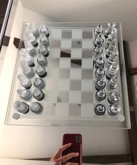 A glass chess set displayed on a reflective, mirrored board