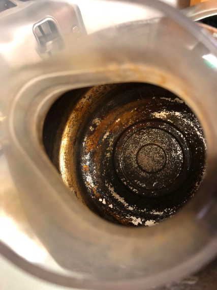 Before: The bottom of a stainless steel coffee pot covered in layers of black and brown coffee stains.