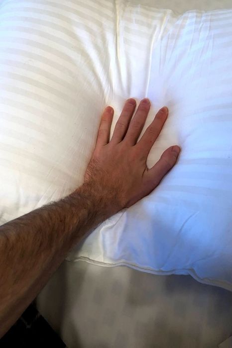 A photo depicting a hand gently pressing down on a pillow.