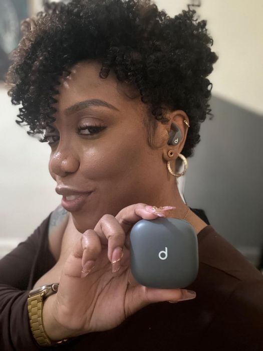 A person smiling while holding a wireless earbuds case in their hand.