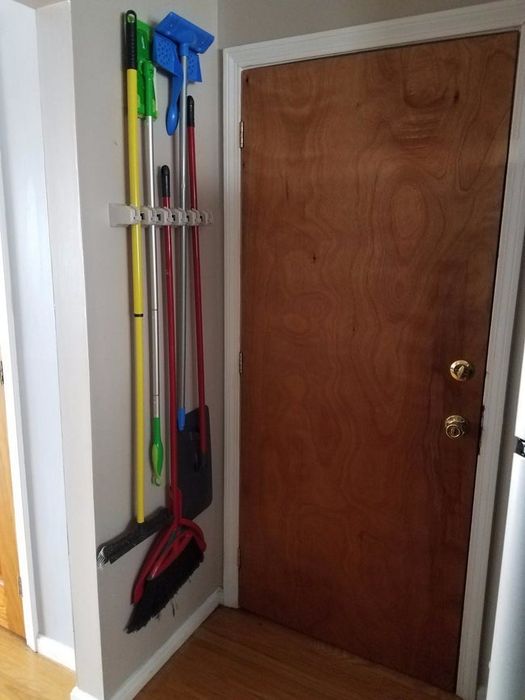 A reviewer showing brooms and swiffers neatly hanging from a small wall-mounted rack behind a door.
