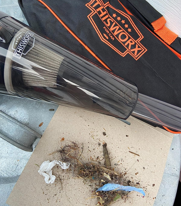 A reviewer's vacuum cleaner, shown with a pile of dirt, twigs, and debris it collected during use.