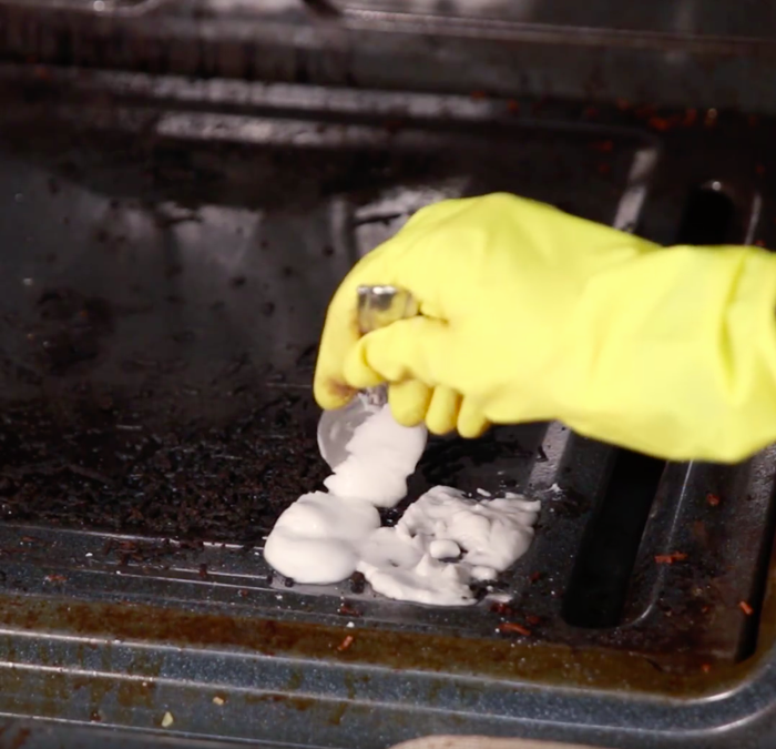 A yellow-gloved hand carefully scoops paste and applies it to the oven door.