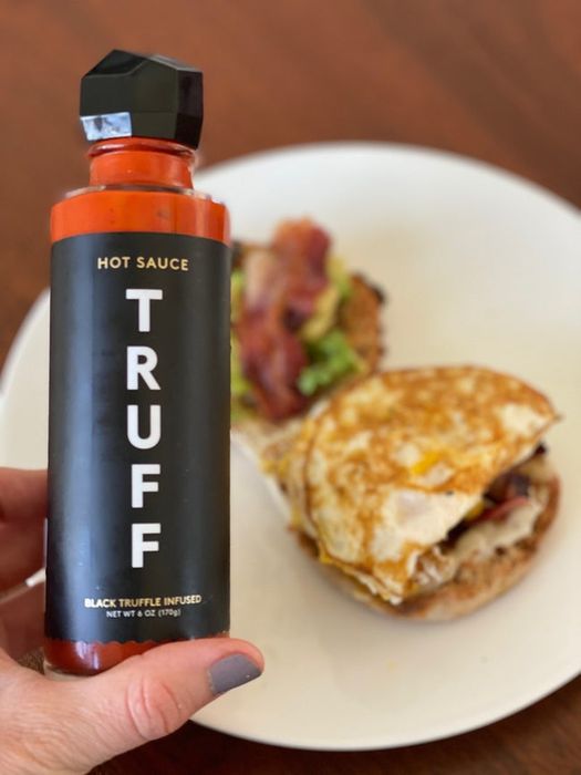 A Mytour writer holding a bottle of Truff Hot Sauce in front of a delicious breakfast sandwich.