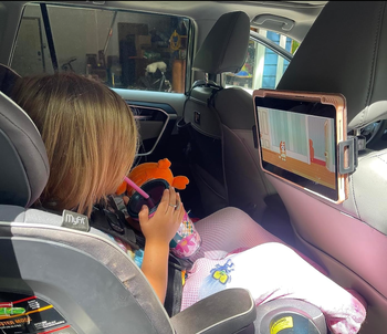 A child in a car seat watching Bluey on an iPad mounted to the back of a seat