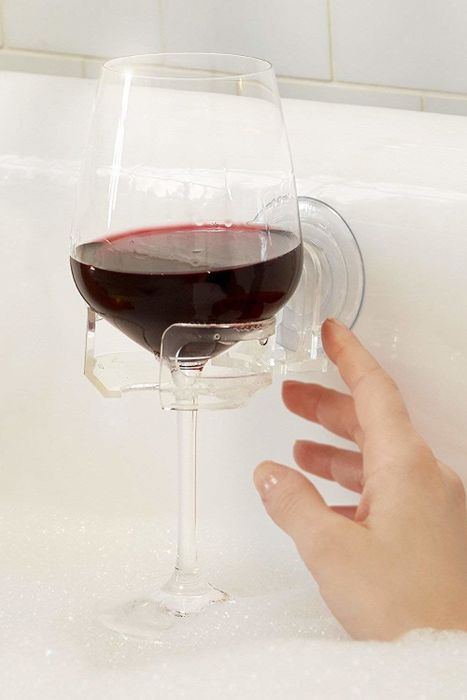 A hand reaching for a wine glass securely placed in a holder mounted on the bathtub wall.
