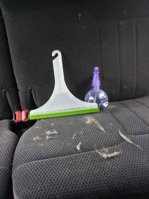 The blogger demonstrated how to use a spray bottle, a squeegee, and gathered clumps of pet hair that had been lifted from the fabric of the upholstered car seat.