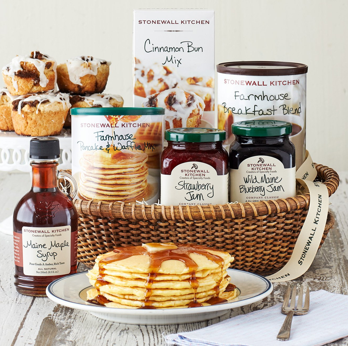 A plate of pancakes served alongside a basket filled with Stonewall Kitchen's maple syrup, pancake and cinnamon bun mix, coffee, and two types of jam.