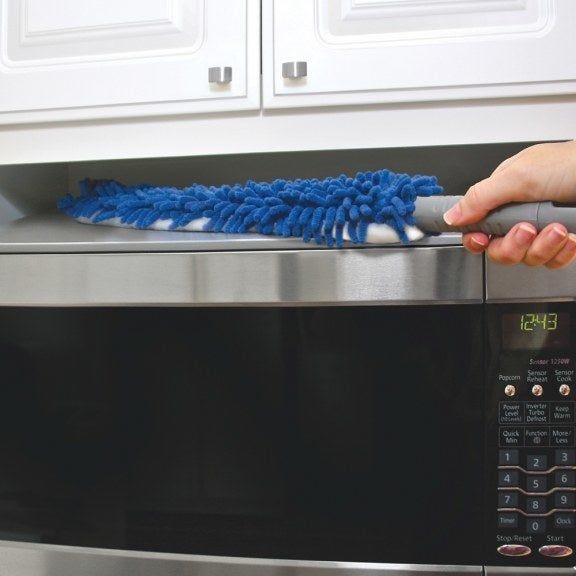 A thin, paddle-shaped, dual-sided duster being used to wipe down the top of a microwave.