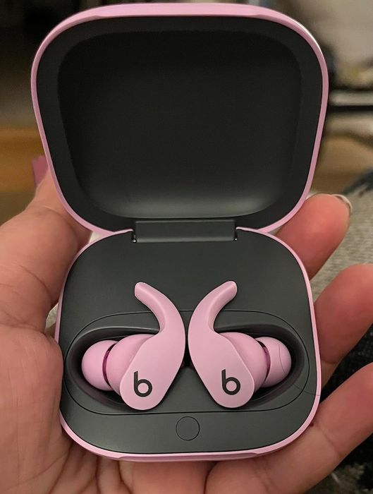 A pair of pink wireless earbuds inside an open charging case, held in a hand, ideal for fitness and active use.