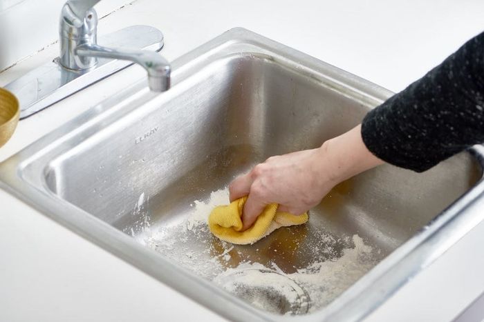 Scrubbing a stainless steel sink with flour for a deep clean.