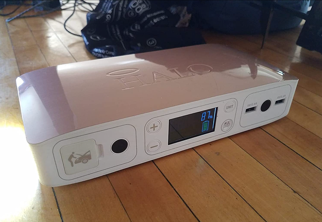 A reviewer's photo of a pale pink rectangular power bank, with a screen showing the inflation percentage of tires