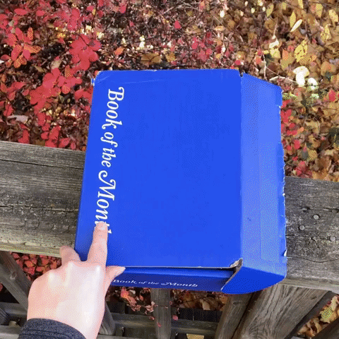 A gif showing a Mytour writer unboxing a blue Book of the Month box to reveal the book inside.
