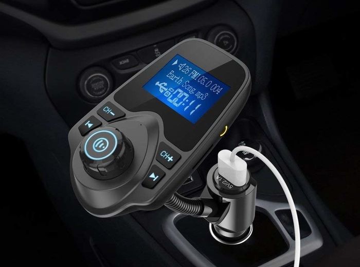 The black audio adapter inserted into a car jack, complete with a small display and buttons to pause or skip songs.
