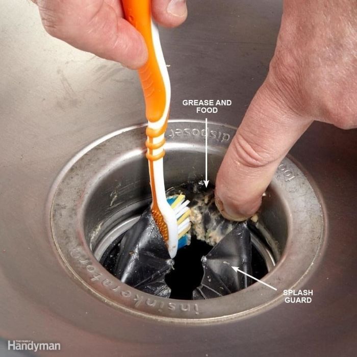 A hand lifting the splash guard of a garbage disposal, revealing grime stuck to the underside.