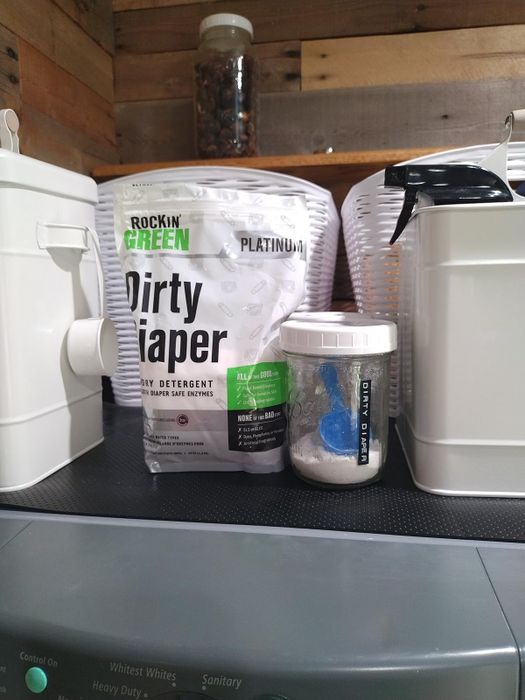 Rockin' Green Platinum Dirty Diaper laundry detergent sits on top of a washing machine beside a jar and other laundry storage containers.