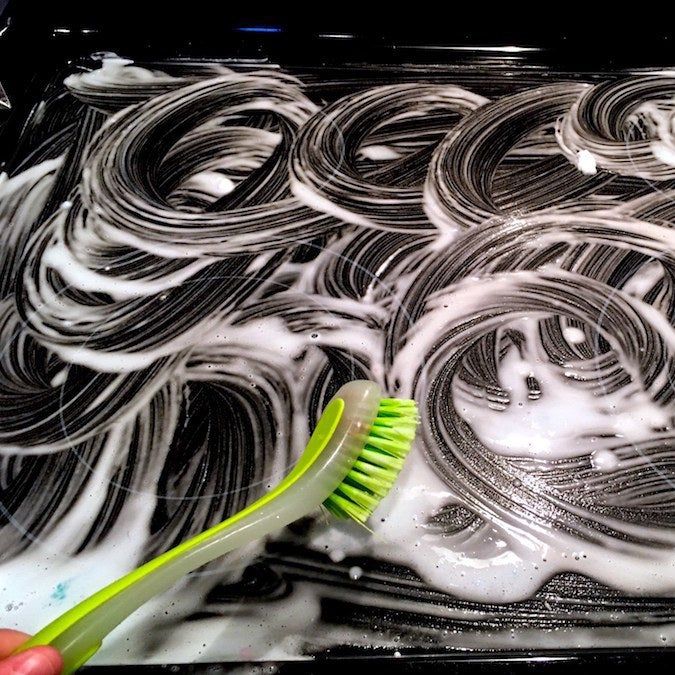 A dish brush on a soapy stovetop, after scrubbing.