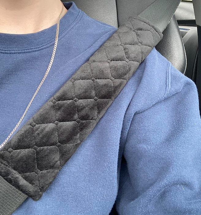 A reviewer showcasing a seatbelt with a black, soft, cross-hatch stitched pad wrapped around the strap at the shoulder.