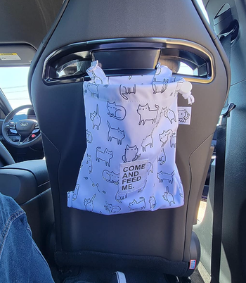The same bag in white, adorned with black outlined cats, hanging from the back of a car seat