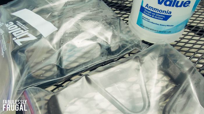 A blogger's stove grates placed inside Ziploc plastic bags, with a bottle of ammonia positioned behind them.