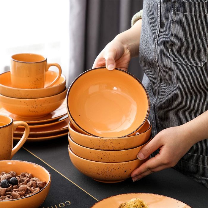 A model holding an orange bowl, surrounded by the rest of the matching orange dinnerware set.