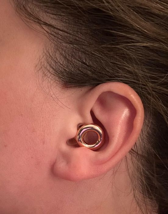 A close-up of an ear adorned with a sleek, round ear cuff featuring a contemporary design