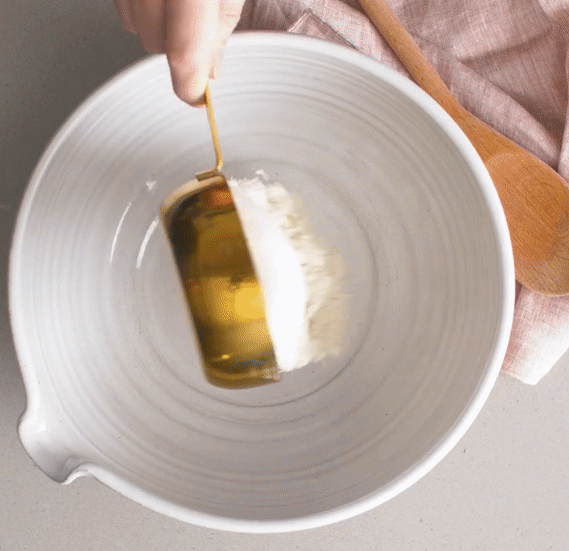A gif showing someone using the gold measuring cups to pour flour and sugar into a mixing bowl with precision.