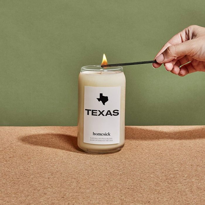 A hand lighting the Texas Homesick candle with a match.