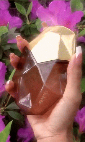A hand holding a faceted perfume bottle with a gold cap surrounded by purple flowers. The bottle has a sleek, geometric design, perfect for a shopping article.