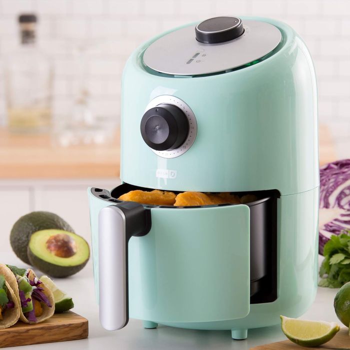 A compact air fryer sitting on a kitchen counter, surrounded by food items, demonstrating the convenience of this appliance for quick and efficient meal preparation
