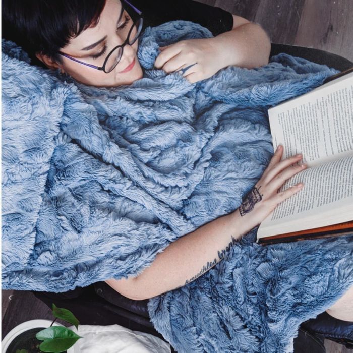A reviewer reading a book while wrapped up in a cozy blue blanket.