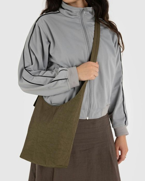 A person dressed in a zip-up jacket and skirt, holding a khaki crossbody tote bag, ideal for casual, everyday use.