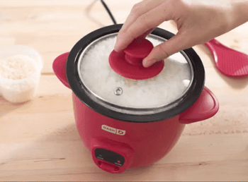 A GIF showing someone lifting the lid off the red rice cooker to reveal perfectly cooked white rice, followed by a spatula scooping the rice.
